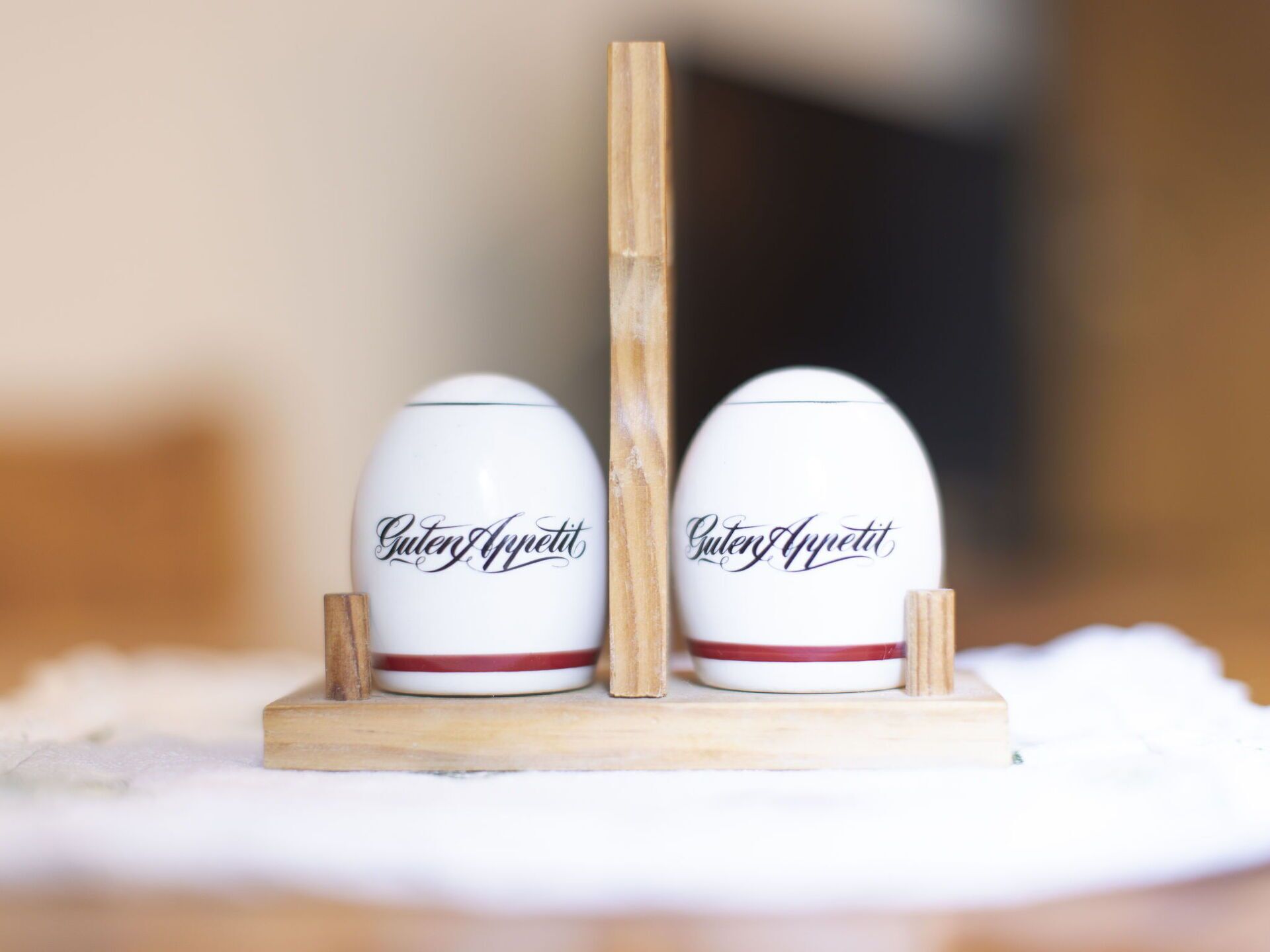 Two white ceramic eggs with red bands and the inscription "Guten Appetit" on a wooden stand.