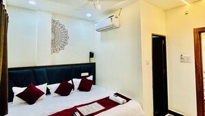 A hotel room with a bed, a ceiling fan, an air conditioning unit, a wall-mounted decorative piece, and a door. - Hotel Shree (Ujjain)