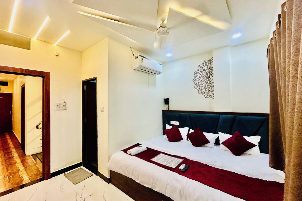 A hotel room with a bed, a ceiling fan, an air conditioning unit, a wall-mounted decorative piece, and a door leading to another room.