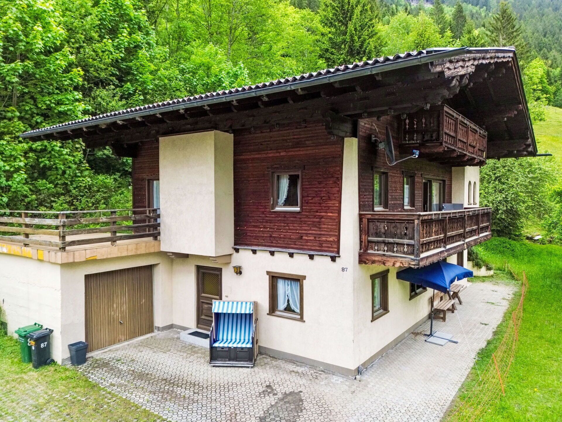 A two-story chalet with a balcony, a covered patio area, and a view of a lush green valley.