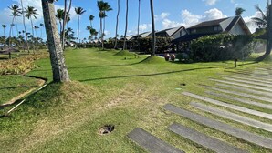 A well-maintained lawn with a wooden pathway, palm trees, and a building with a sloped roof. - Malawi Resort (Ipojuca)