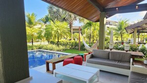 A covered outdoor area with a pool, seating, and greenery.