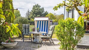 Een terras buiten met een stenen tafel en twee stoelen, een gestreepte stoel, en een bloempot met plant.
