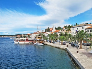 Ein Küstenort mit Booten im Hafen, einer gepflasterten Uferpromenade und traditionellen Gebäuden mit roten Ziegeldächern.