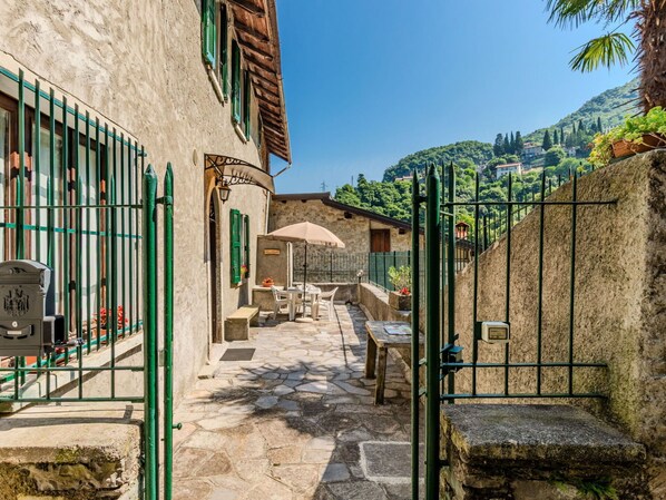A narrow stone-paved courtyard with outdoor seating, a stone wall, and a gate.