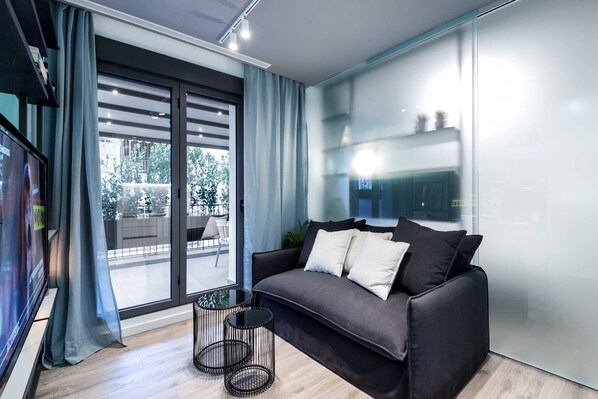 A modern living room with a dark grey sofa, two white cushions, and a glass table.