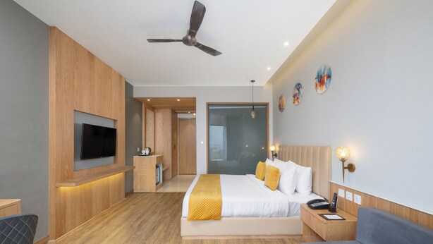 A modern hotel room with a large bed, a TV, a desk, and a ceiling fan. - Regenta Marrievilla Ambala (Ambala)