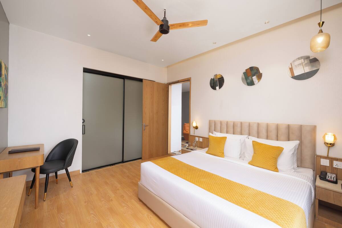 A modern hotel room with a large bed, a desk, a chair, and a ceiling fan.