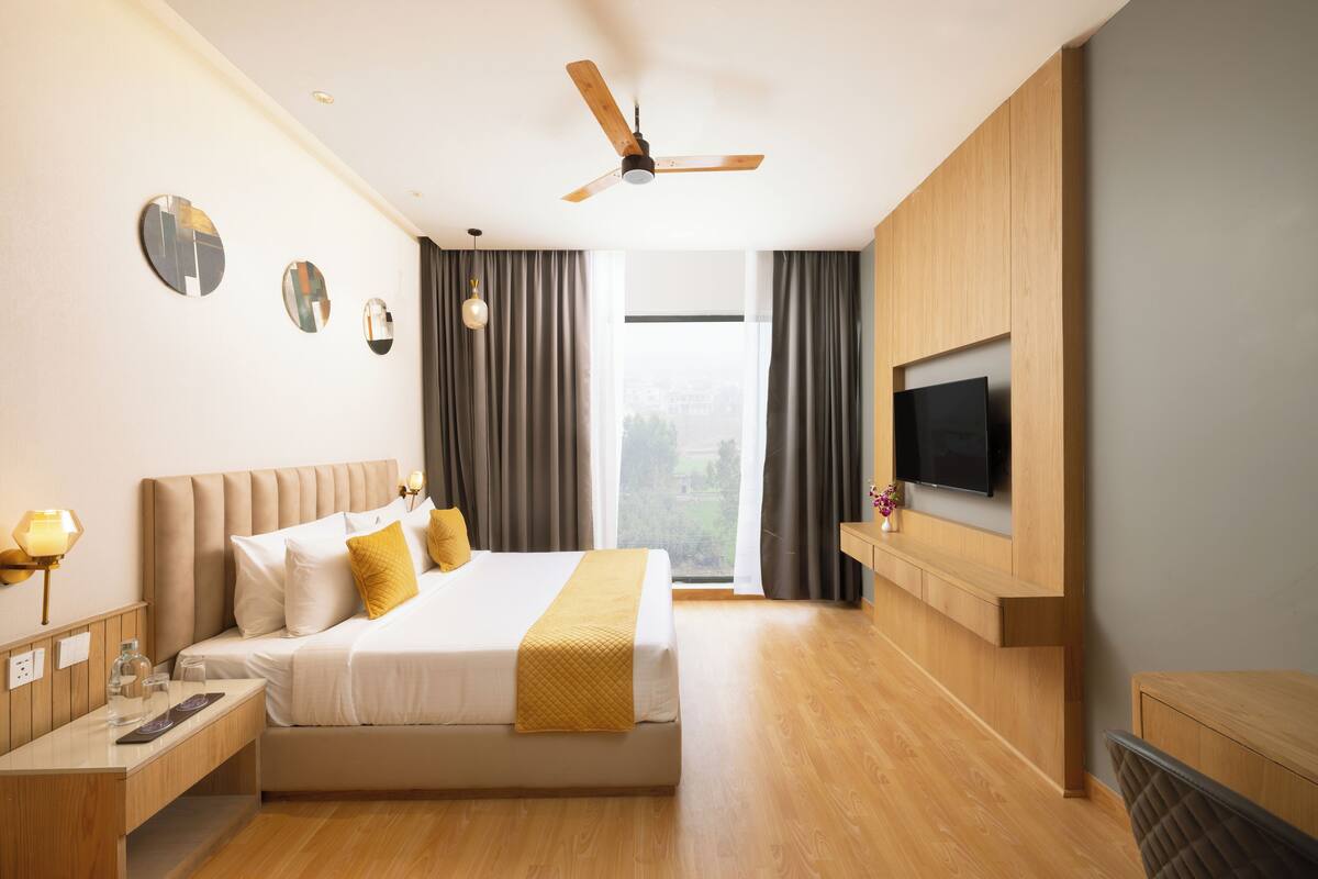 A modern hotel room with a large bed, a ceiling fan, a TV mounted on the wall, and a view of the outdoors.