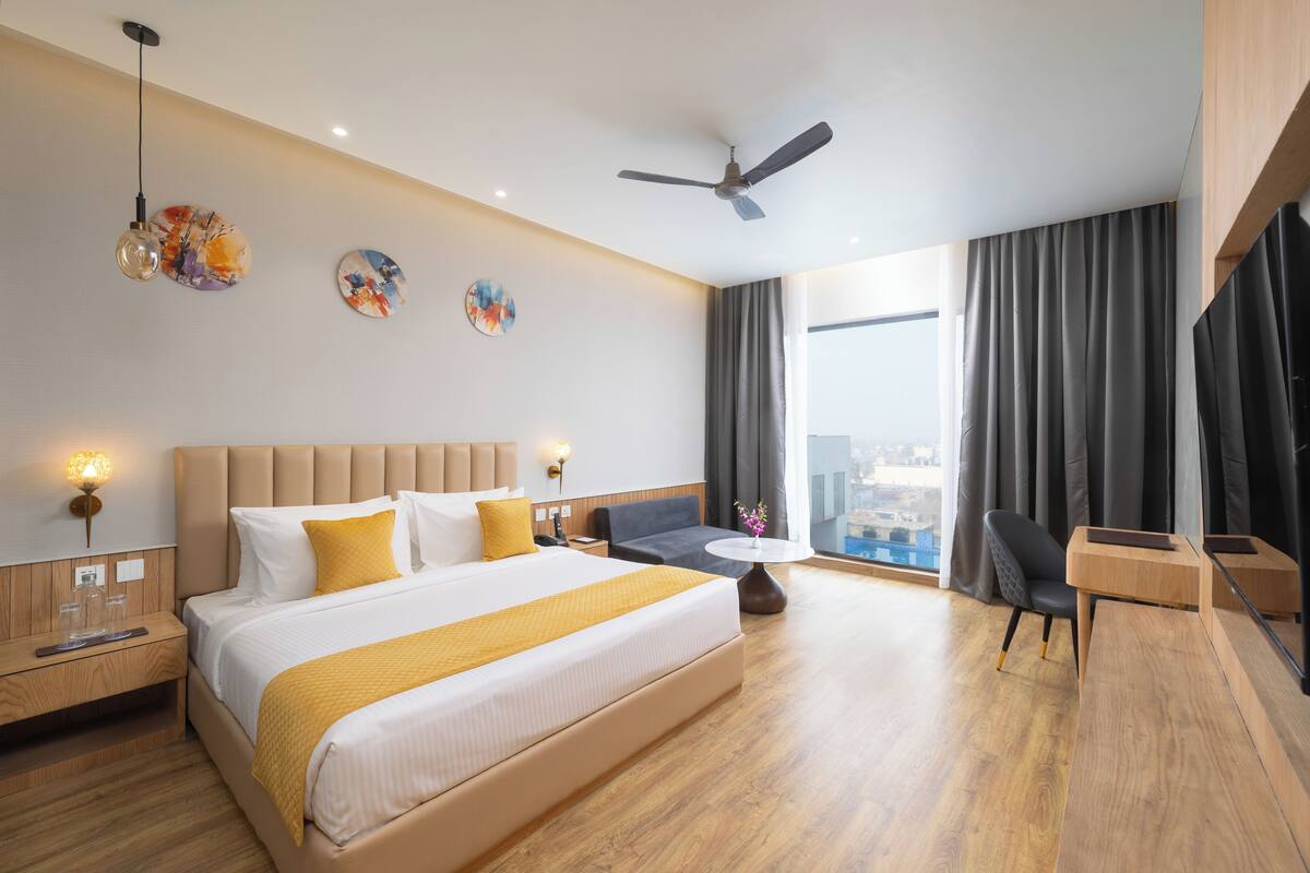 A modern hotel room with a large bed, a desk, a chair, a round table, and a city view.