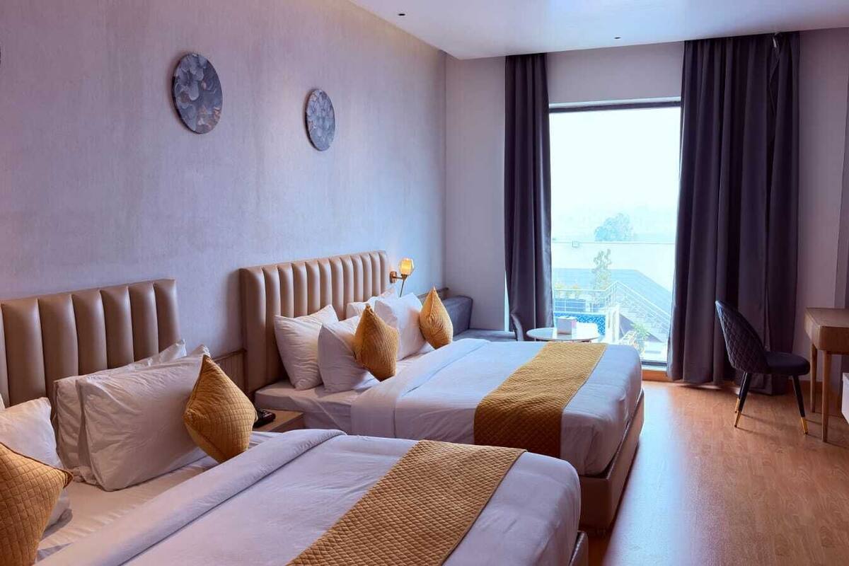 A hotel room with two beds, a desk, and a view of the city.