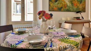 A dining table set with plates, glasses, and a vase of flowers, with a painting on the wall and a window with shutters. - Bright in Saint Ursula (Bergamo)