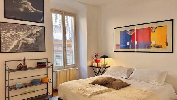 A bedroom with a bed, a metal shelf unit, a window with shutters, and two framed artworks. - Bright in Saint Ursula (Bergamo)