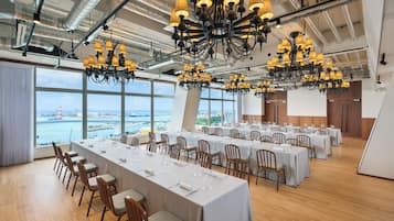 A conference room with multiple tables, chairs, and chandeliers, overlooking a scenic view.