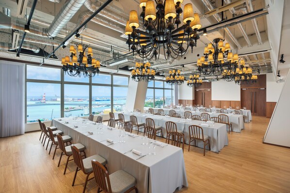A conference room with multiple tables, chairs, and chandeliers, overlooking a scenic view. - South Gate Hotel Okinawa Naha Tomari Port (Direct Access to Tomarin) (Naha)