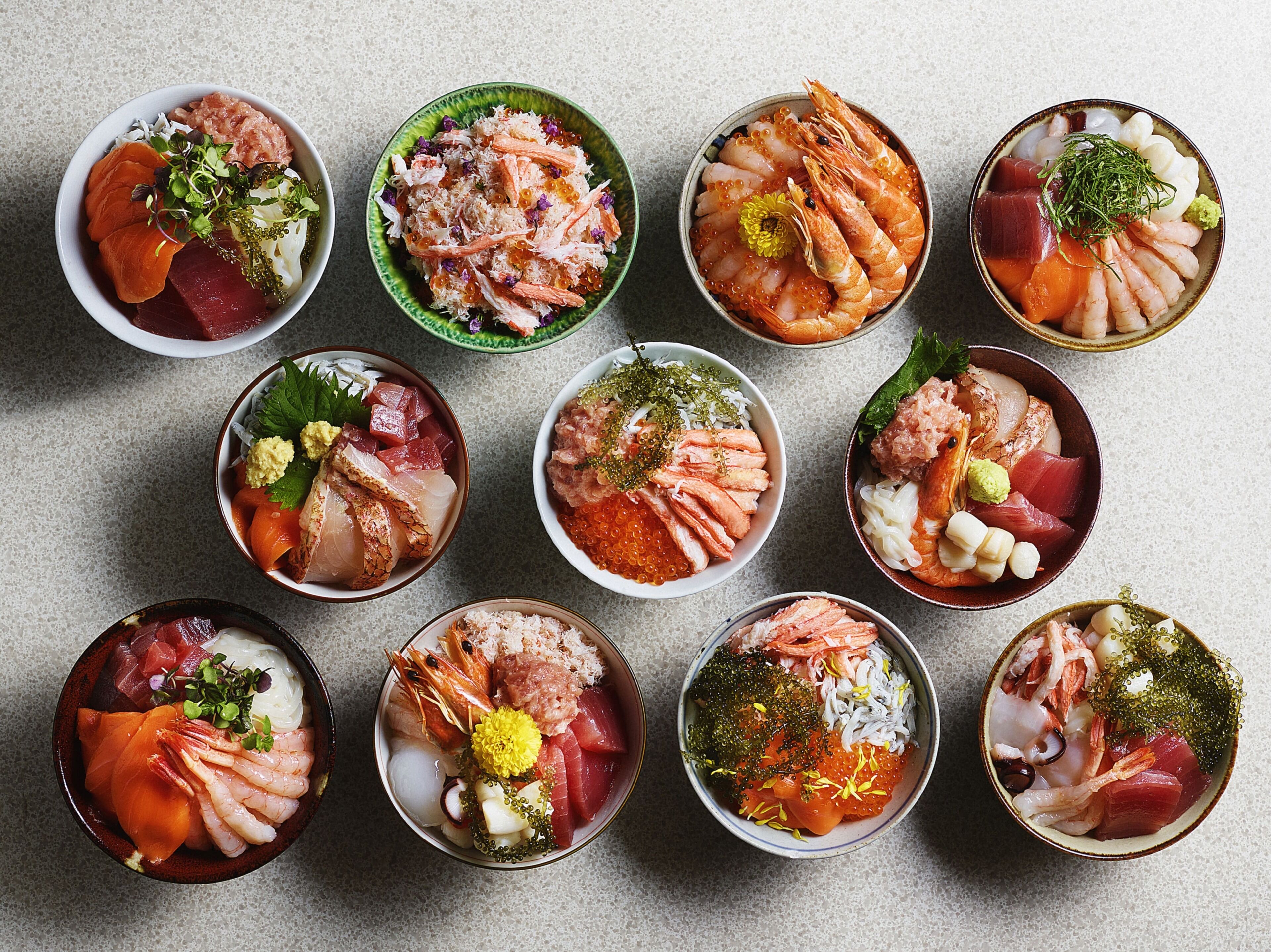 A variety of bowls containing different types of sashimi and seafood.