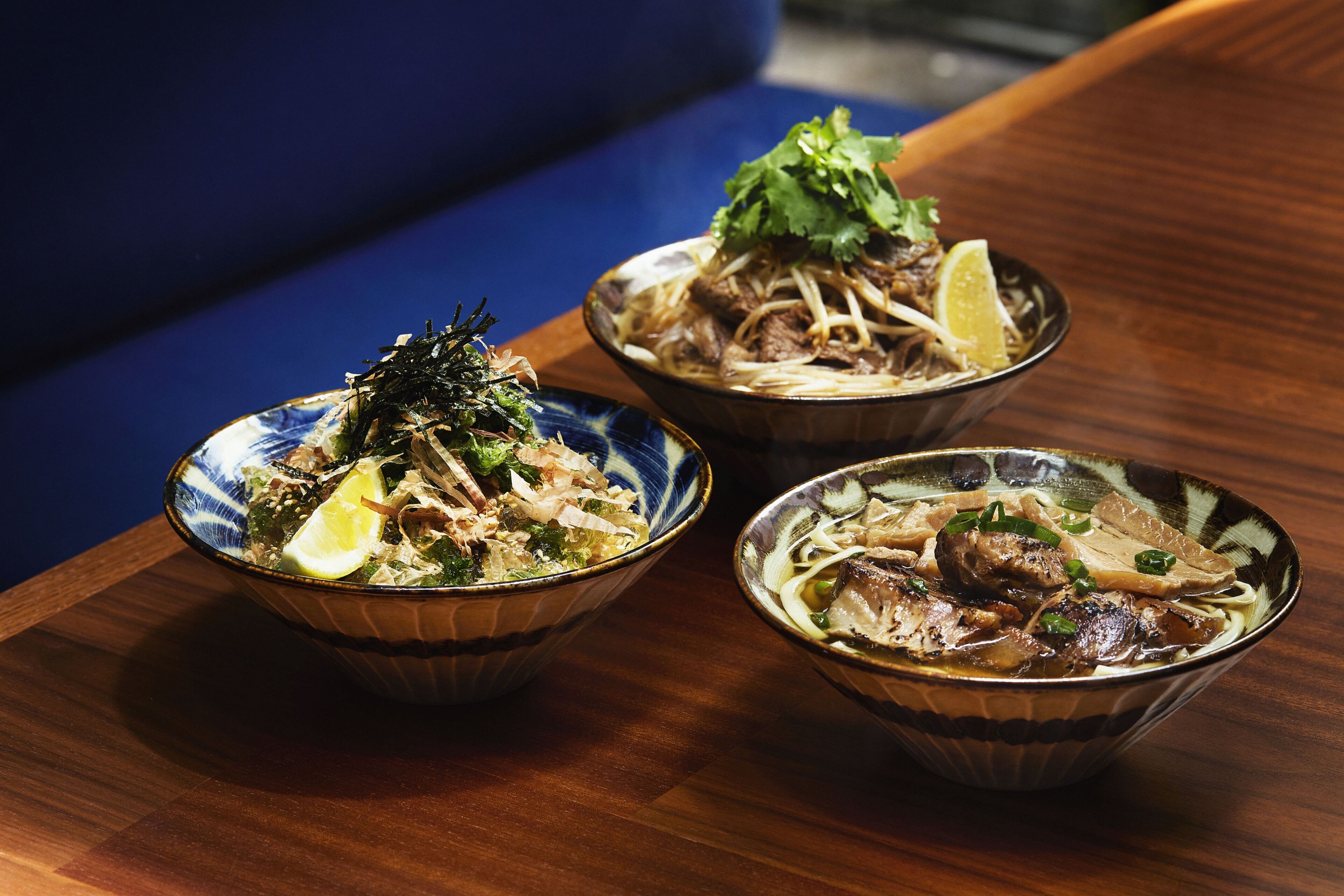 Three bowls of noodle soup with various toppings on a wooden table.