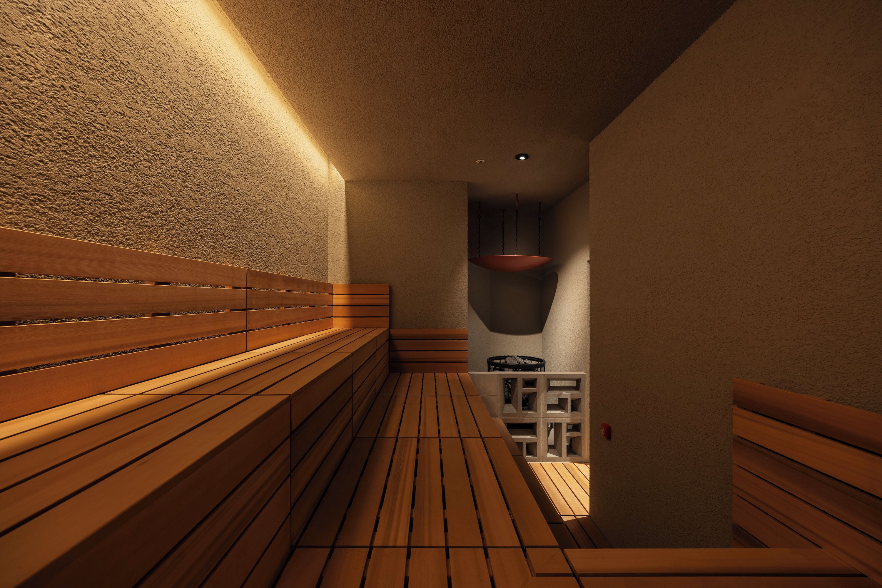 A narrow hallway with wooden benches and a small seating area with a chair and a shelf.