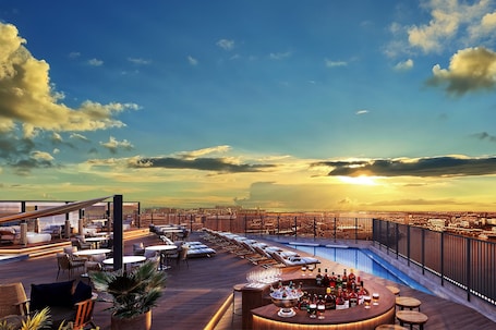 A rooftop bar with a pool, lounge chairs, and a bar area with bottles and glasses.. South Gate Hotel Okinawa