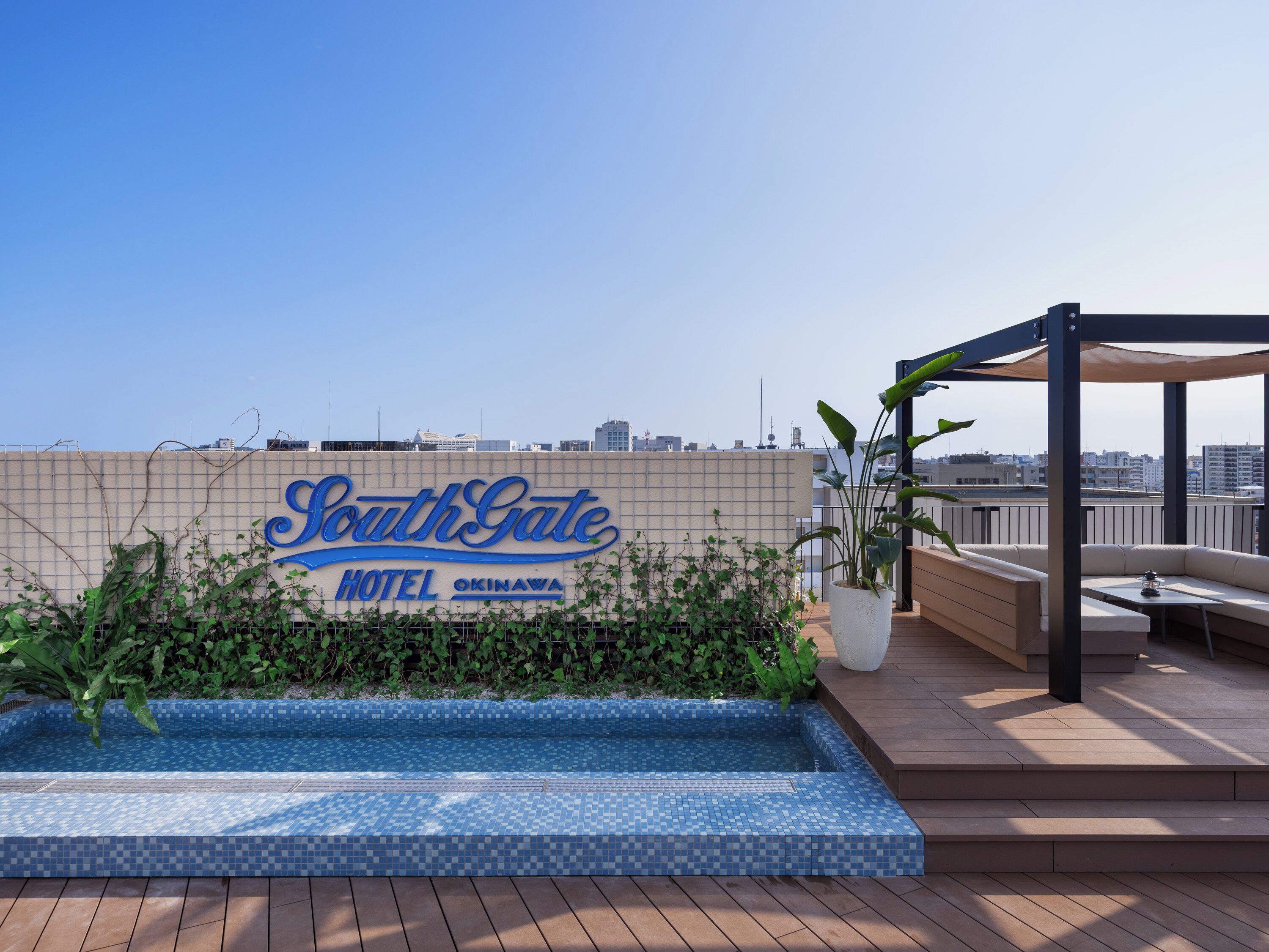 A rooftop pool area with a sign for SouthGate Hotel Okinawa, surrounded by plants and a seating area.