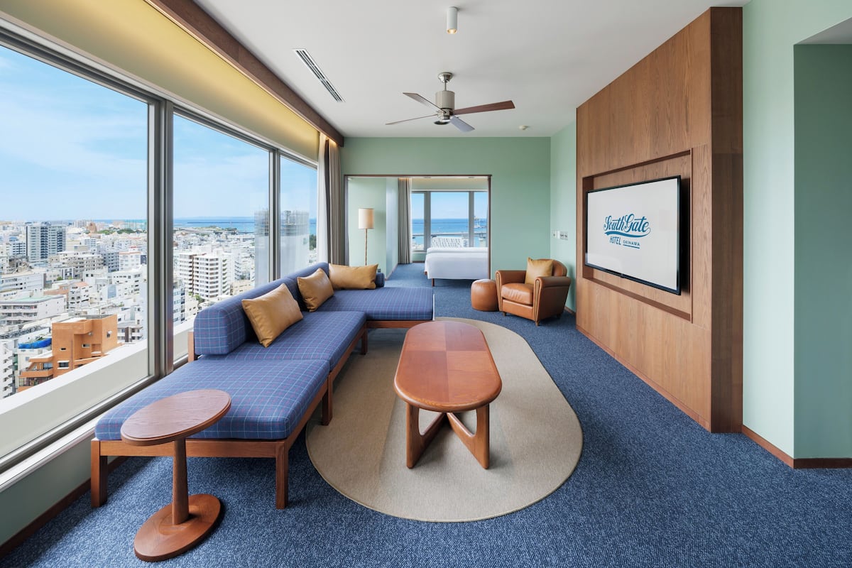 Una habitación de hotel con un ventanal grande, una cama, un sofá, una mesa y un televisor.