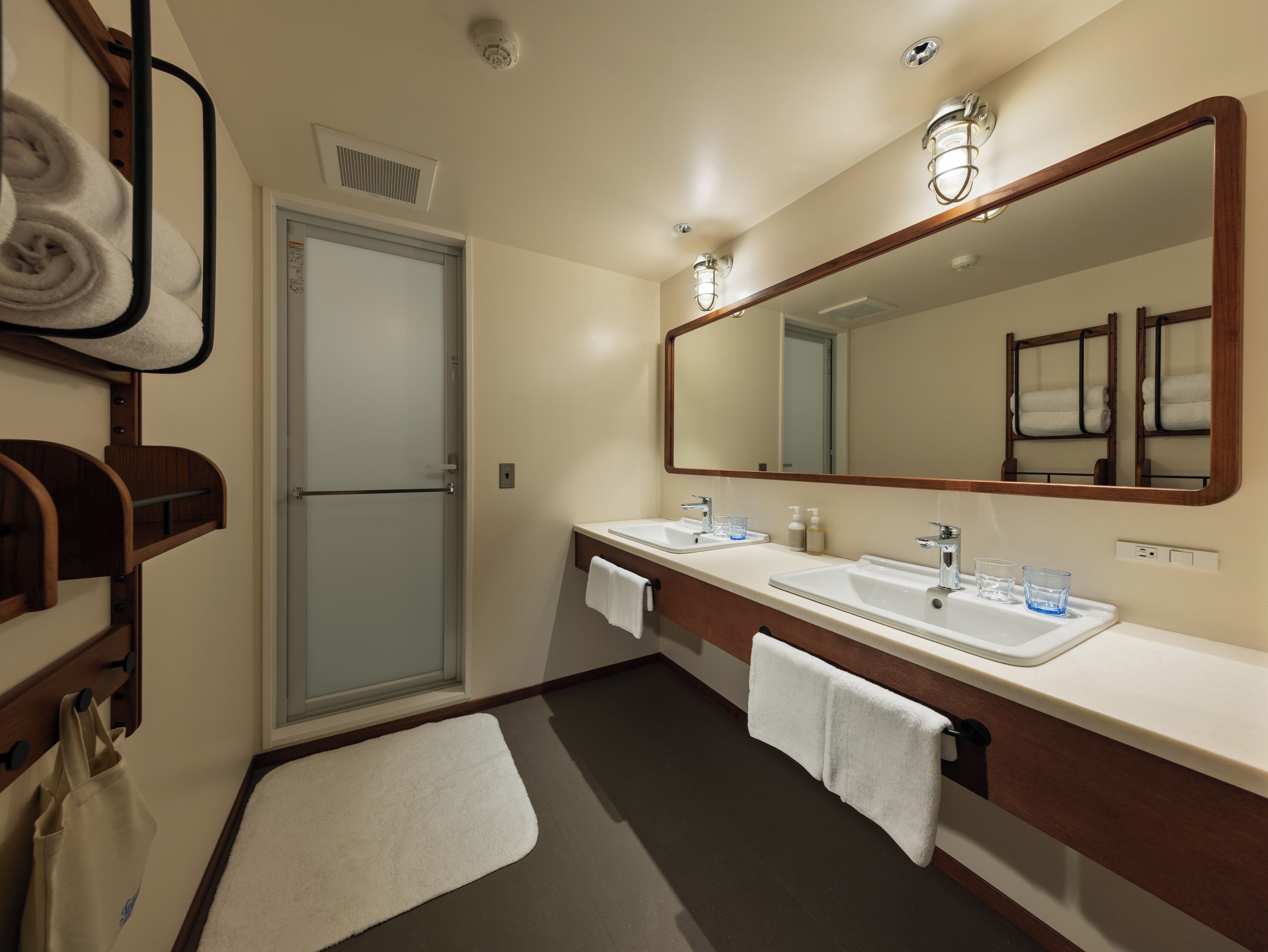 A hotel bathroom with a shower, two sinks, a large mirror, and towels.