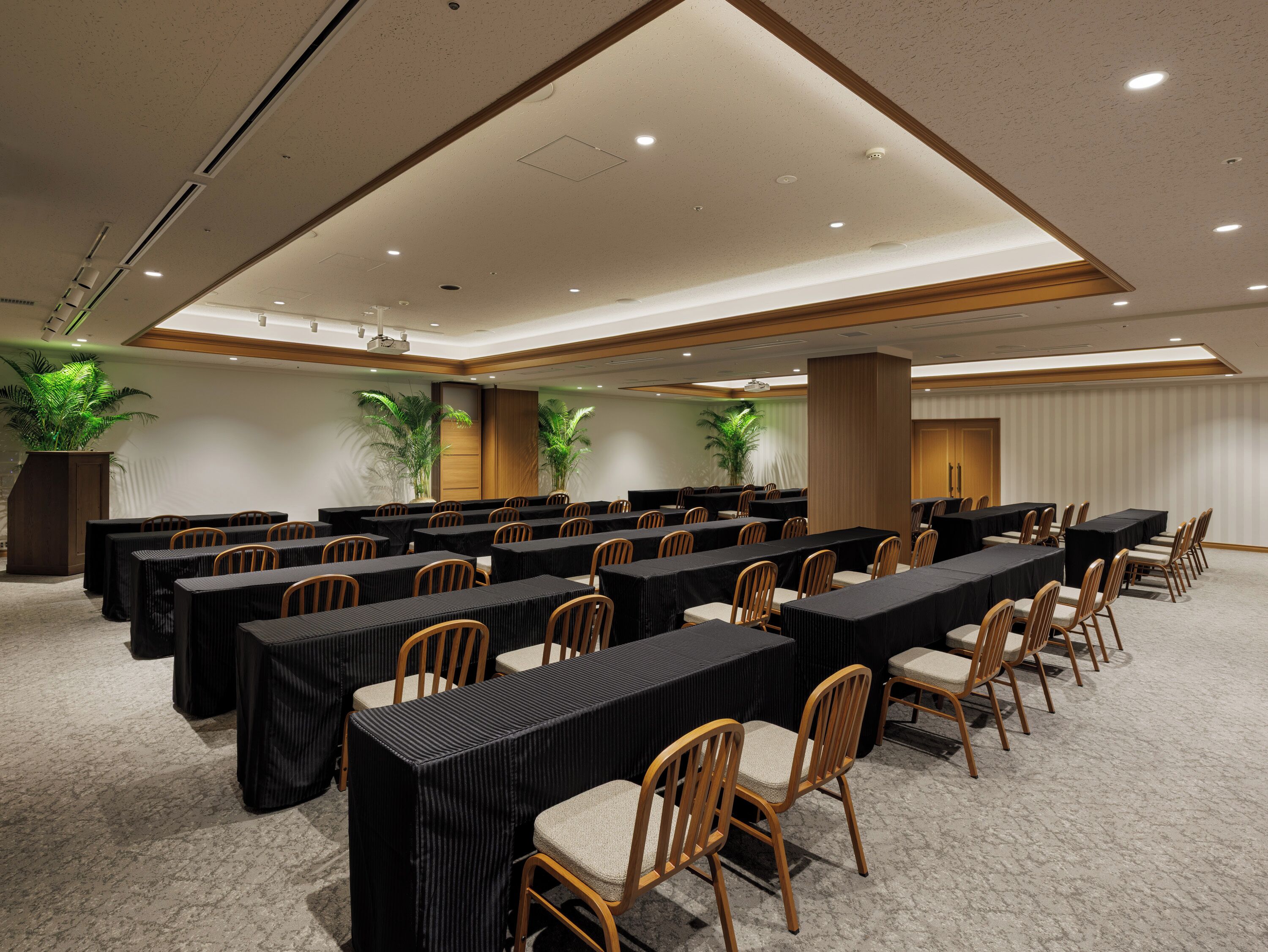 A conference room with long tables, chairs, and potted plants.