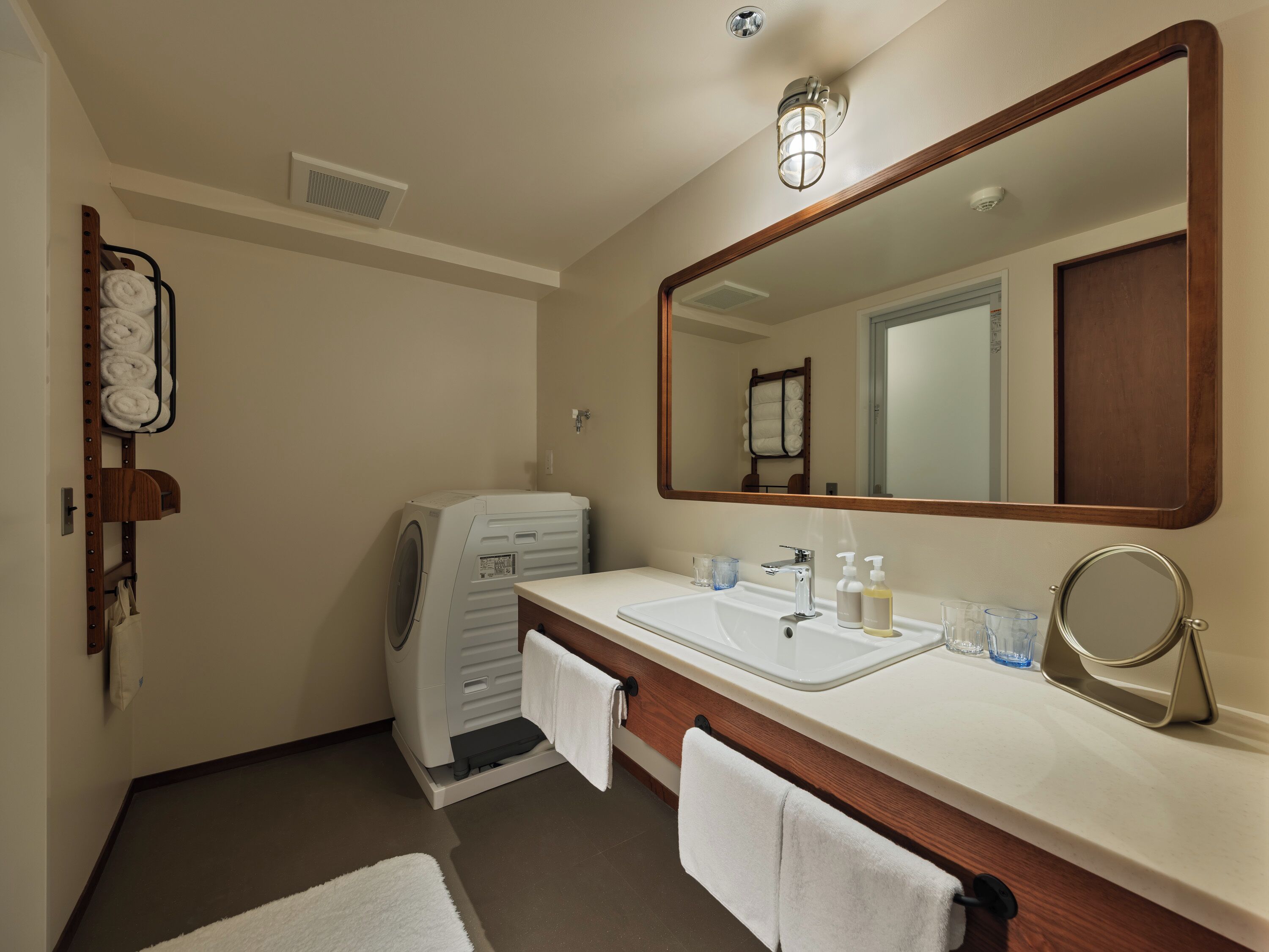 A bathroom with a large mirror, a sink, a towel rack, and a washing machine.