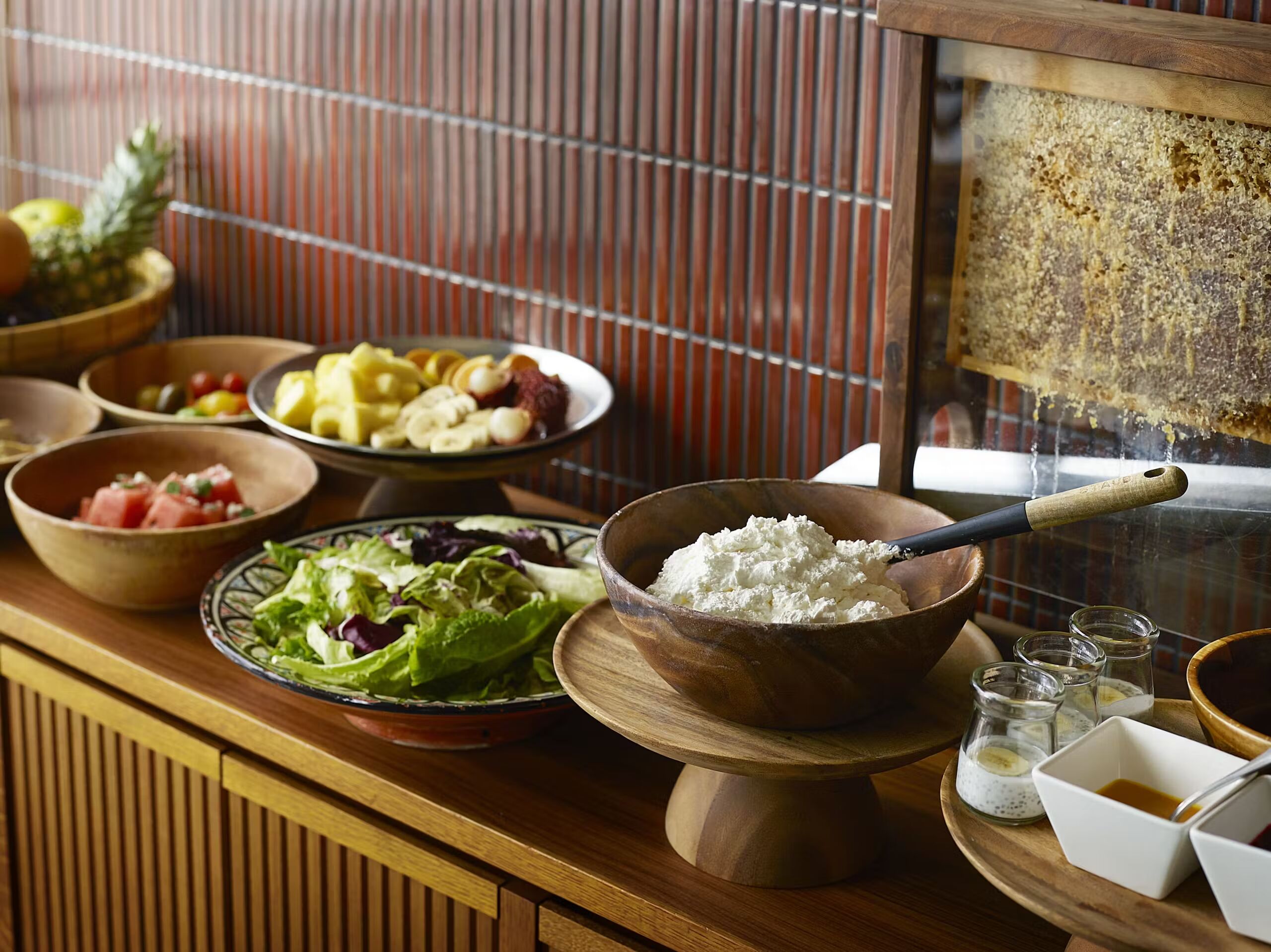 A wooden buffet table with various dishes including a bowl of cottage cheese, a salad, and bowls of fruit and vegetables.