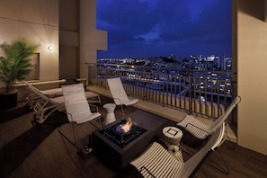 Un balcón con una chimenea, sillones de descanso y vistas de la ciudad de noche.
