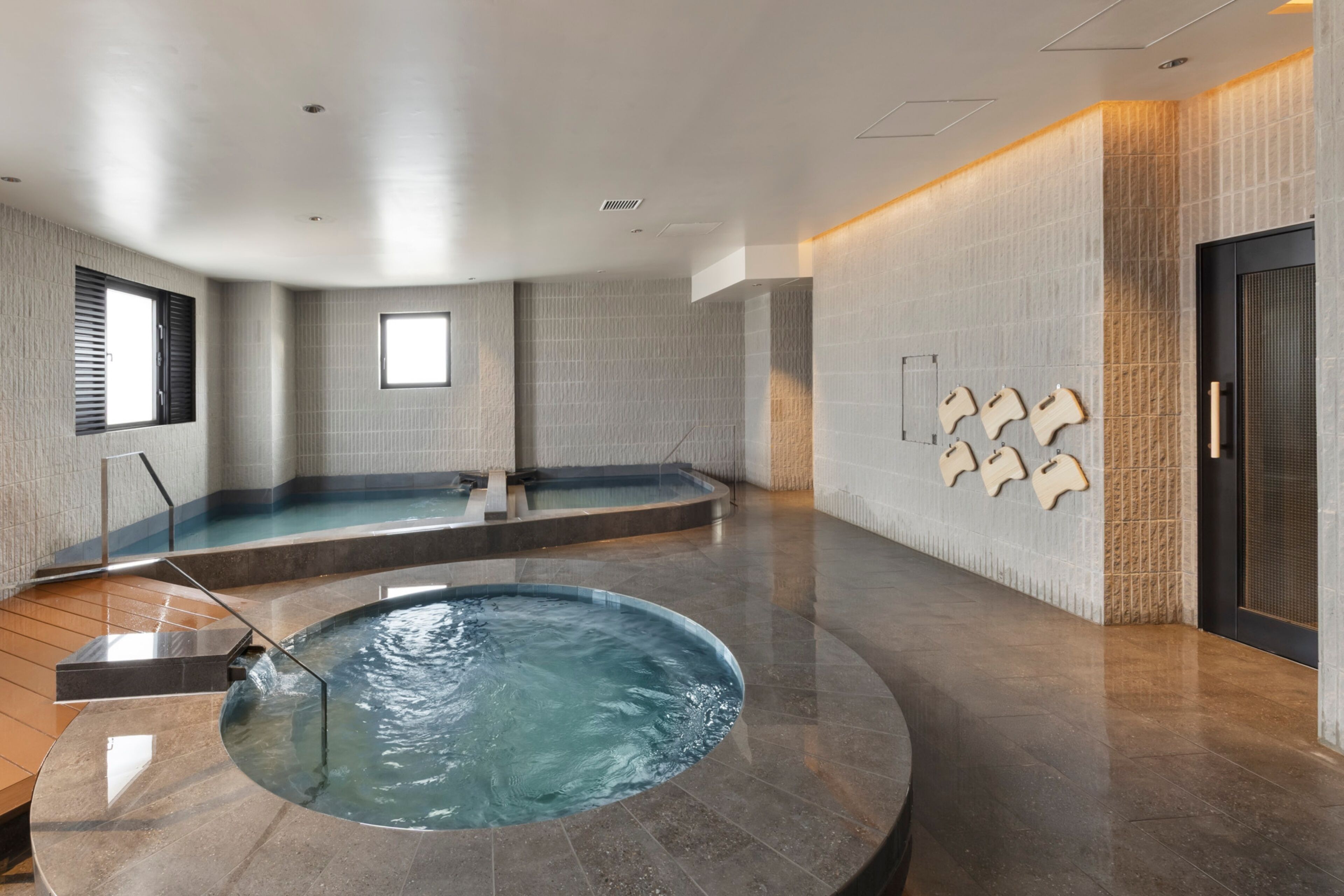 Une piscine intérieure moderne dotée d’un jacuzzi circulaire, d’un espace douche et d’un panneau de revêtement en bois fixé au mur.