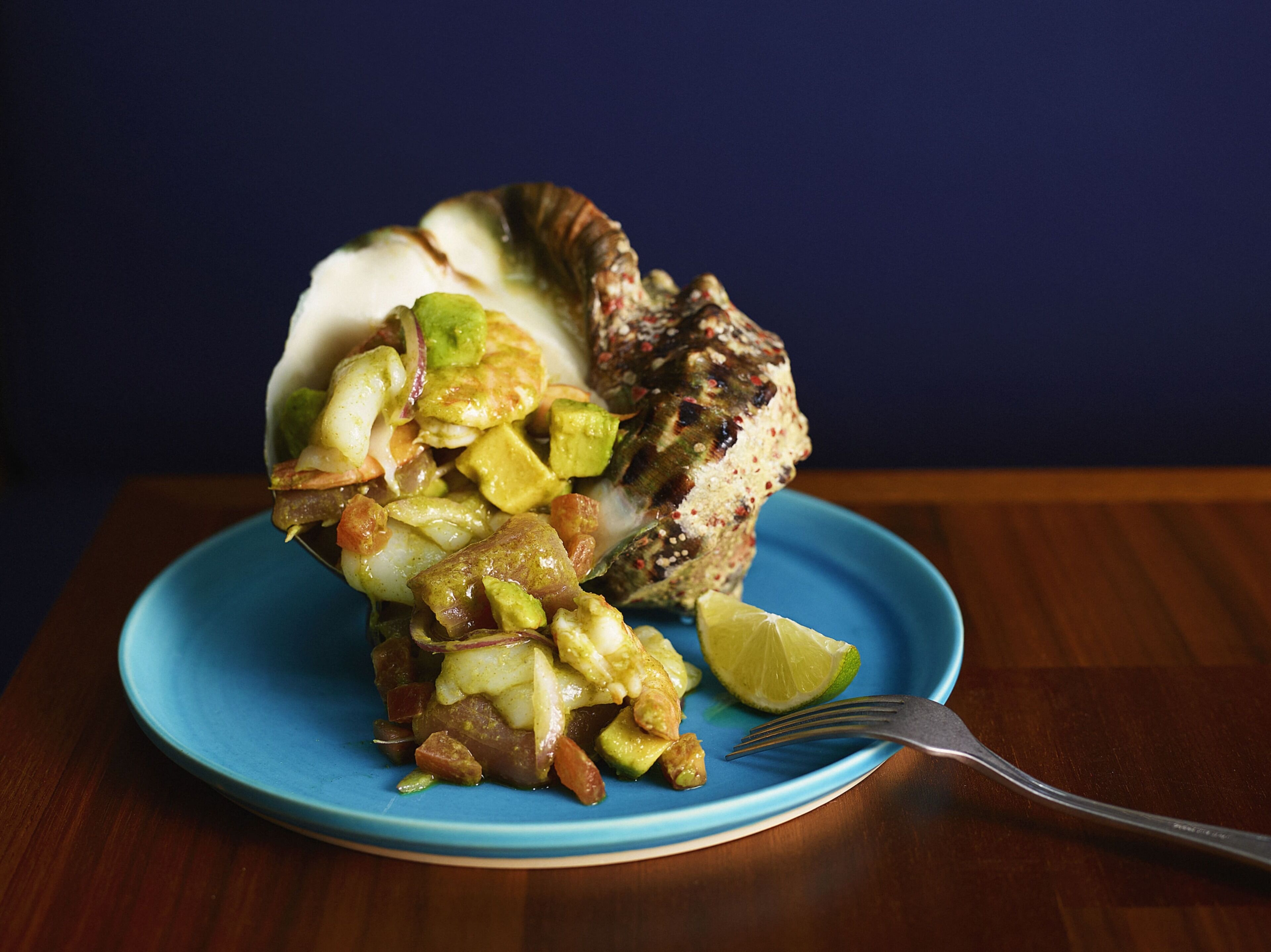 A plate with a food item, a fork, and a lime wedge on a blue plate.