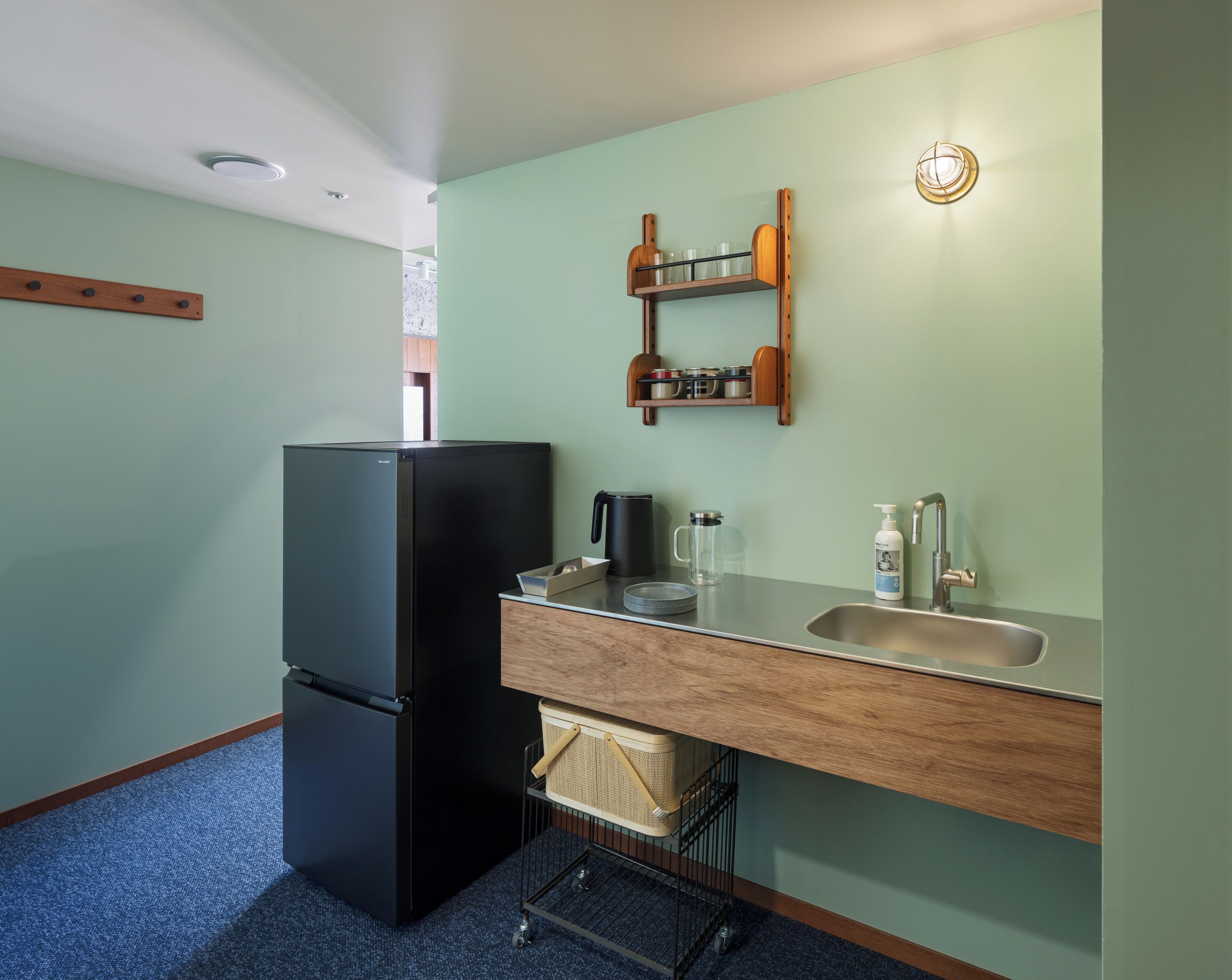 Eine kleine Küche mit einem schwarzen Kühlschrank, einer Holz Arbeitsplatte, einem Spülbecken und einem Regal mit Küchenutensilien.