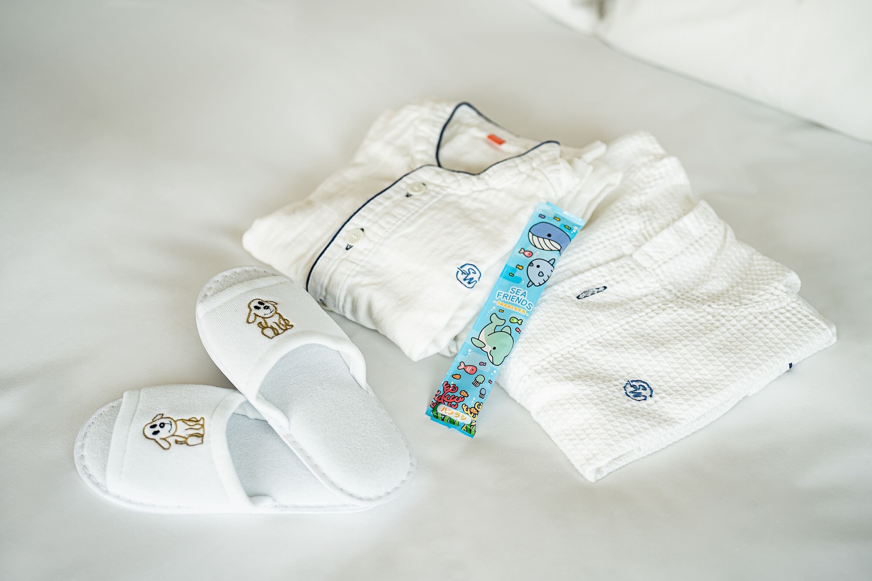 A neatly arranged set of baby clothes and slippers on a white bed.