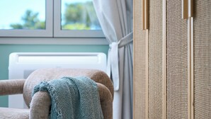 A room with a window, a chair with a blanket, and a wall with a textured panel. - Bougainvillea Bliss (Σκαλα)