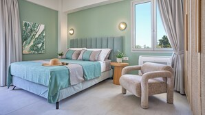 A bedroom with a bed, a chair, a bedside table, a window, and a wall-mounted light fixture. - Bougainvillea Bliss (Σκαλα)