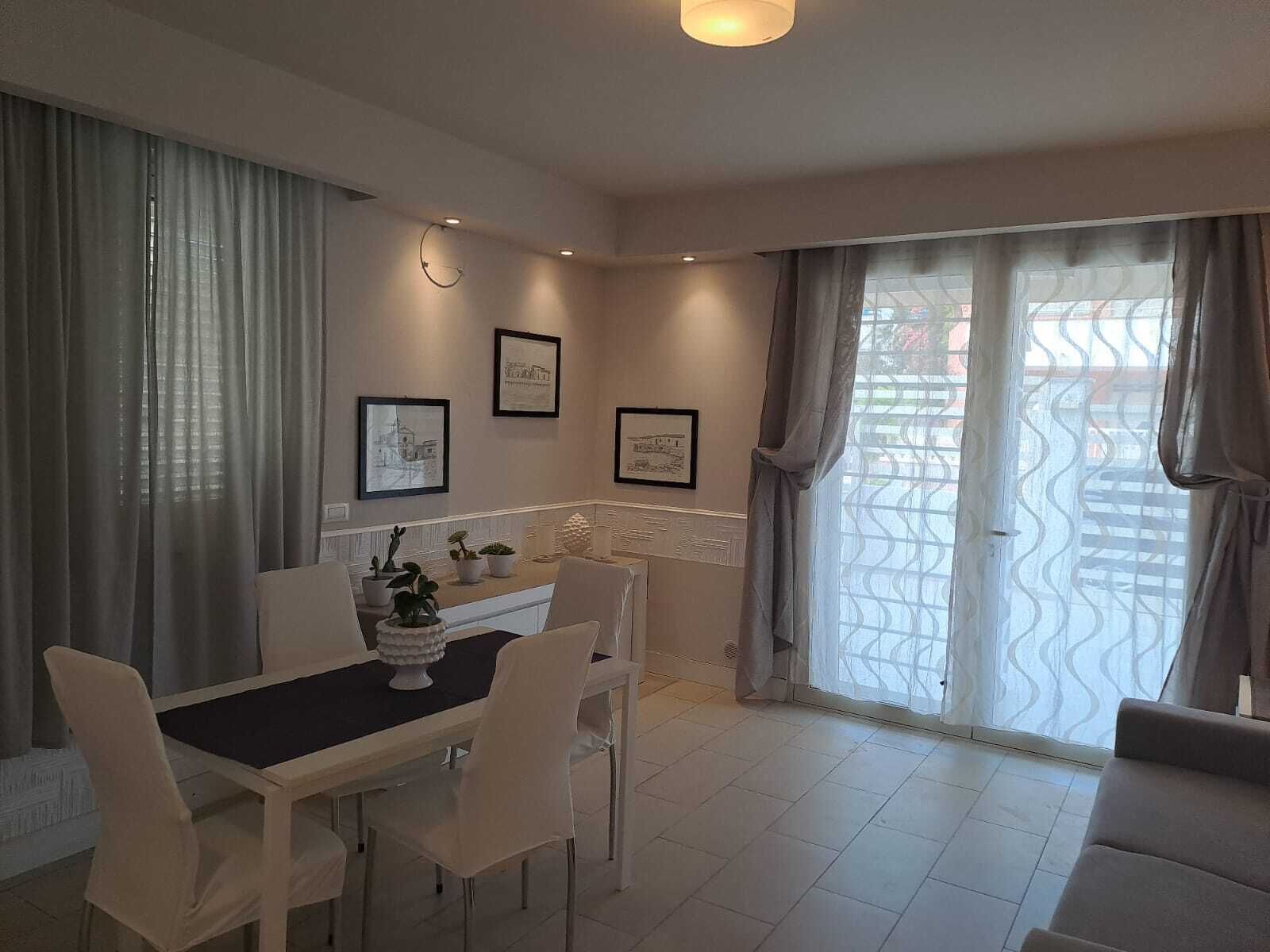 Een moderne eetruimte met een tafel en stoelen, kunstwerken aan de muur en uitzicht door een raam met gordijnen met een patroon.