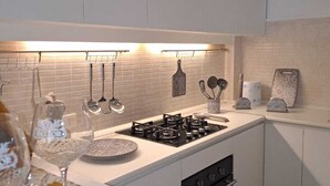 A modern kitchen with white cabinets, a gas stove, and hanging utensils. - Casa Rosa di Sicilia Marzamemi (Marzamemi)