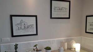 A modern kitchen with white cabinetry, a countertop with potted plants, and framed artwork on the wall. - Casa Rosa di Sicilia Marzamemi (Marzamemi)
