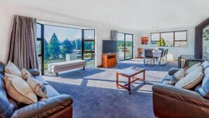 A spacious living room with a large window, a flat-screen TV, a sofa, a coffee table, and a dining area with chairs. - Enjoy 180° views of Lake Tekapo (Lake Tekapo)