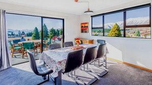 A dining area with a table set for four, large windows with a mountain view, and a modern pendant light. - Enjoy 180° views of Lake Tekapo (Lake Tekapo)