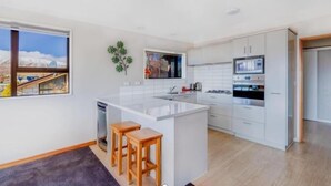 A modern kitchen with white cabinetry, a central island with stools, and a view of a mountainous landscape through a window. - Enjoy 180° views of Lake Tekapo (Lake Tekapo)