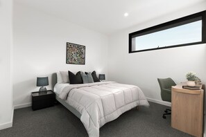 Un dormitorio moderno con una cama, un escritorio, una silla, una ventana y una obra de arte en la pared.