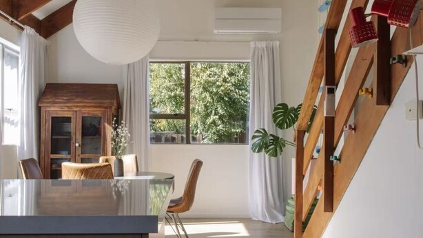 Amplia habitación con techo de madera, zona de comedor con mesa de vidrio y escalera con barandilla de madera.