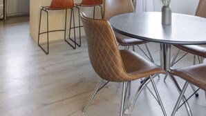Una cocina moderna con vigas de madera, un comedor con sillas de metal y un ventanal con vistas a árboles.