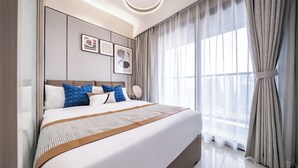Una habitación de hotel moderna con una cama grande, un cabecero con altavoces integrados y un amplio ventanal con cortinas traslúcidas.
