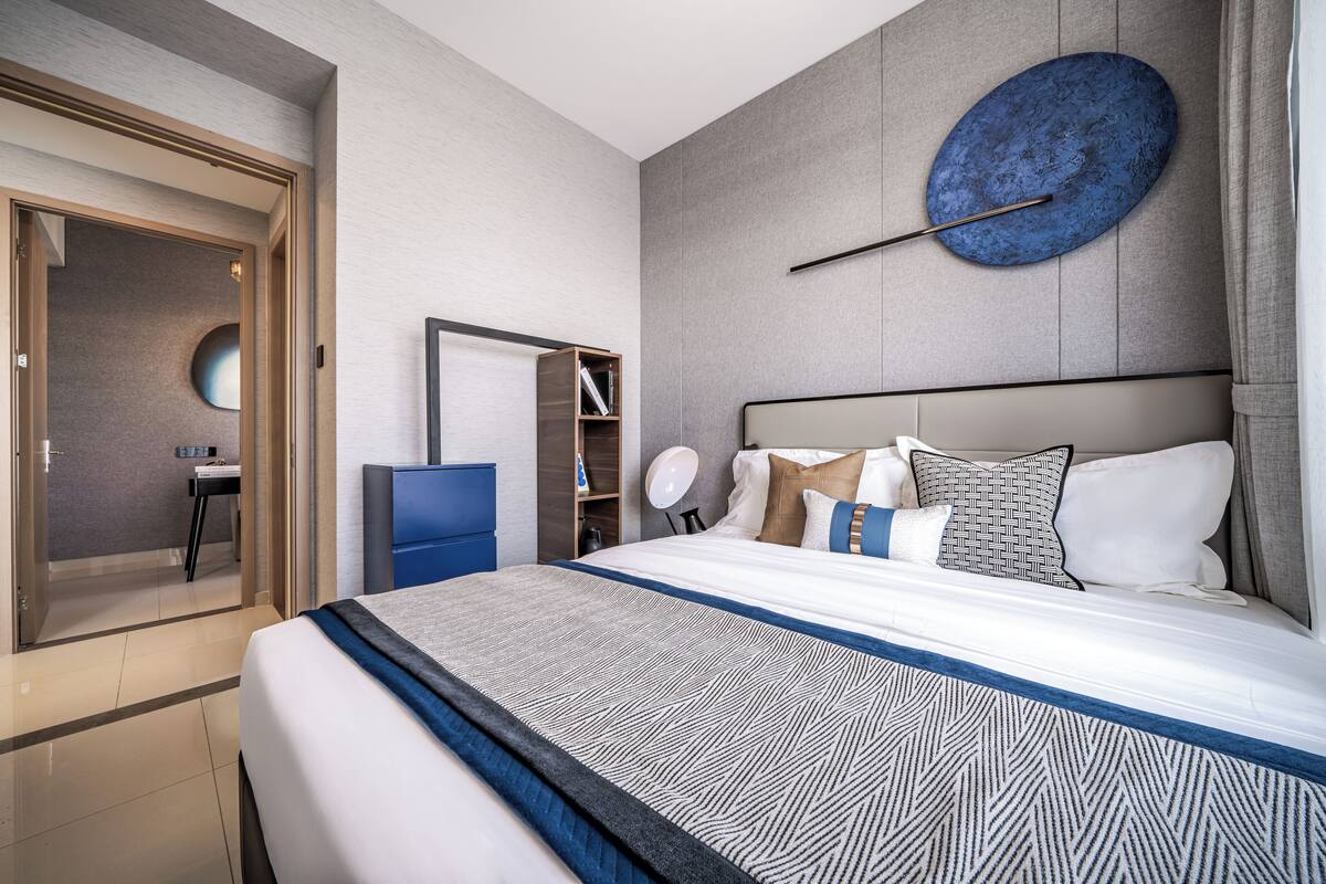A modern hotel room with a large bed, a bedside table, a mirror, and a wall-mounted circular artwork.