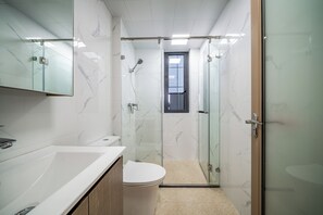 Ein Badezimmer mit einer Duschkabine, einer Toilette und einem Waschbecken mit Spiegel.