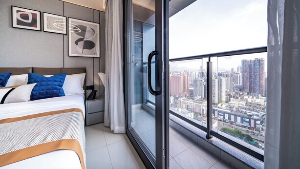 Habitación de hotel moderna con un ventanal que ofrece vistas a la ciudad, una cama bien hecha con ropa de cama azul y blanca, y arte abstracto en la pared.