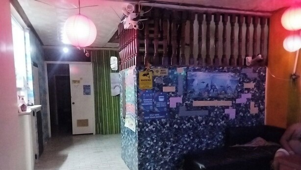 A hallway with a tiled floor, a green door, a wall with various notices, and a black sofa.